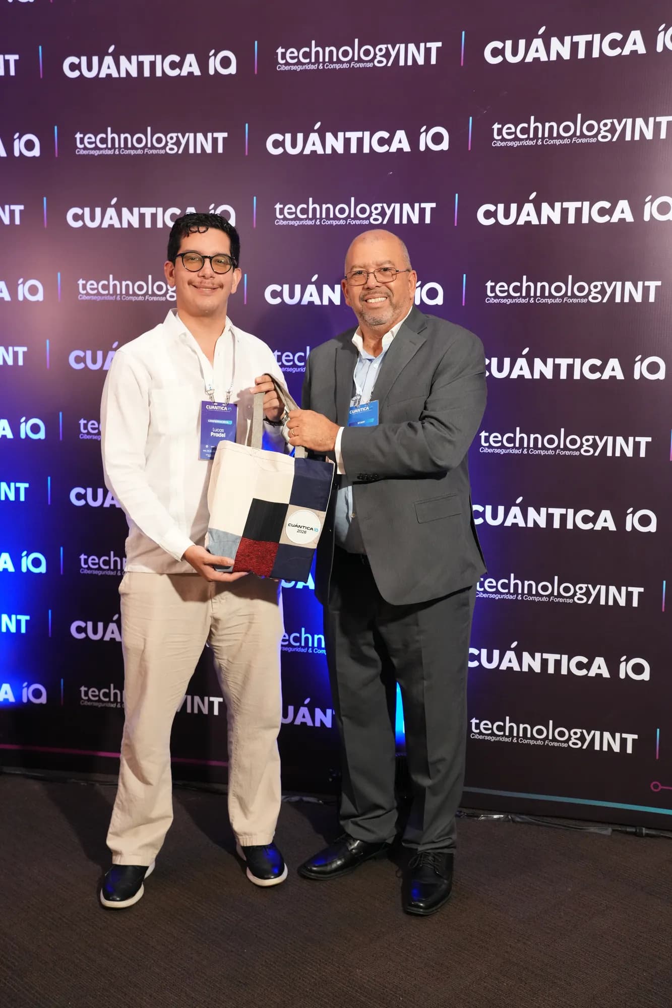 Lucas Pradel receiving a commemorative CuánticaIA 2026 gift from an event organizer in front of the congress backdrop.
