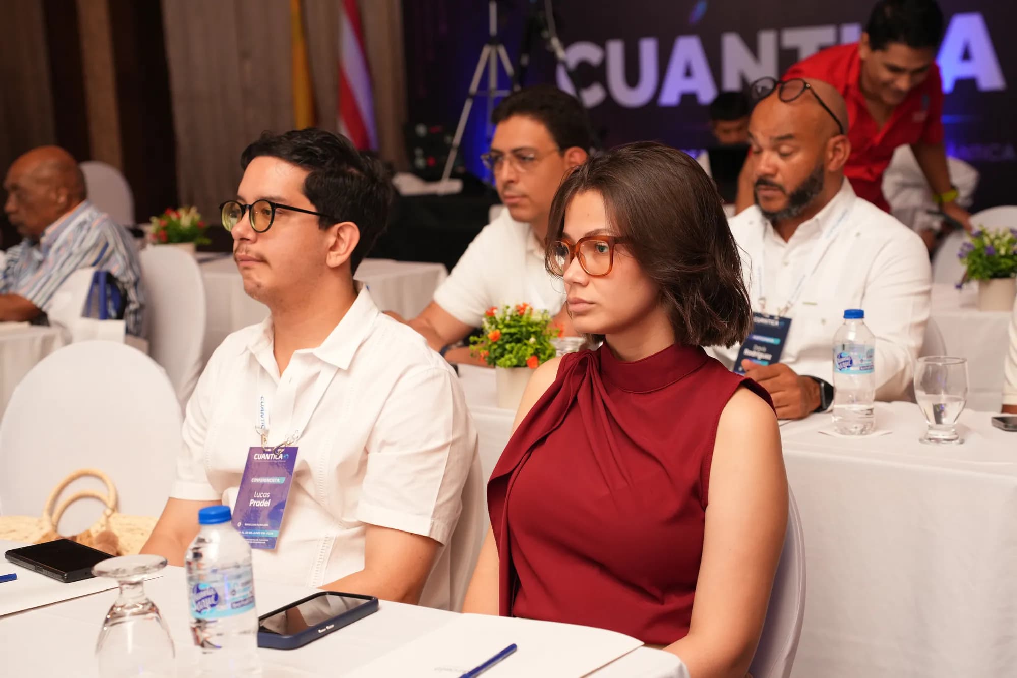 Lucas Pradel seated among attendees at CuánticaIA 2026, wearing a lanyard badge marked 'Conferencista'.